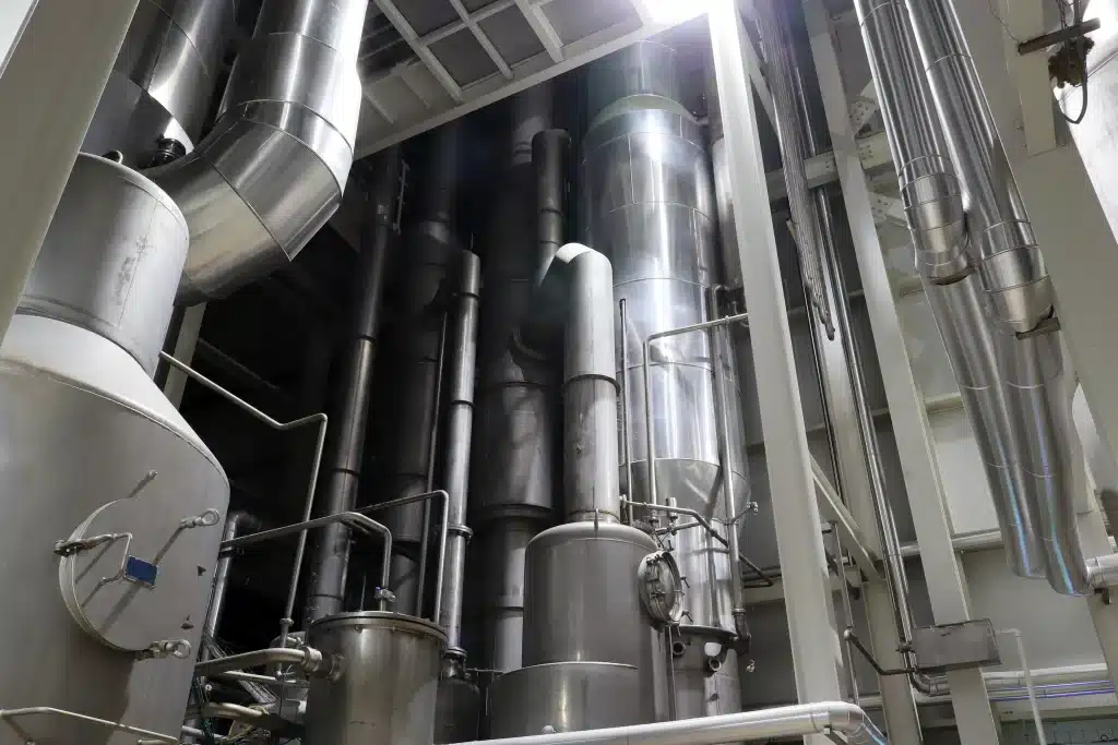 Interior view of an industrial facility featuring a centrifugal spray dryer. The image shows large metallic cylindrical structures with pipes and ductwork intertwined, indicative of a complex mechanical system used for spray drying processes.