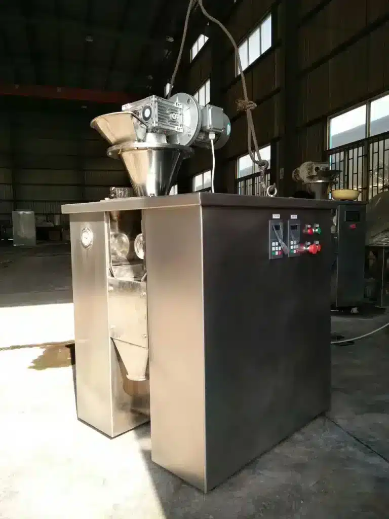 A Dry Compression Granulator with a stainless steel body, control panel, and a top-mounted hopper, situated in an industrial workshop setting.