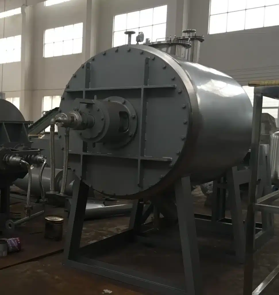 An industrial Paddle Dryer with large cylindrical chambers and external equipment, in a manufacturing facility with high ceilings and natural light.