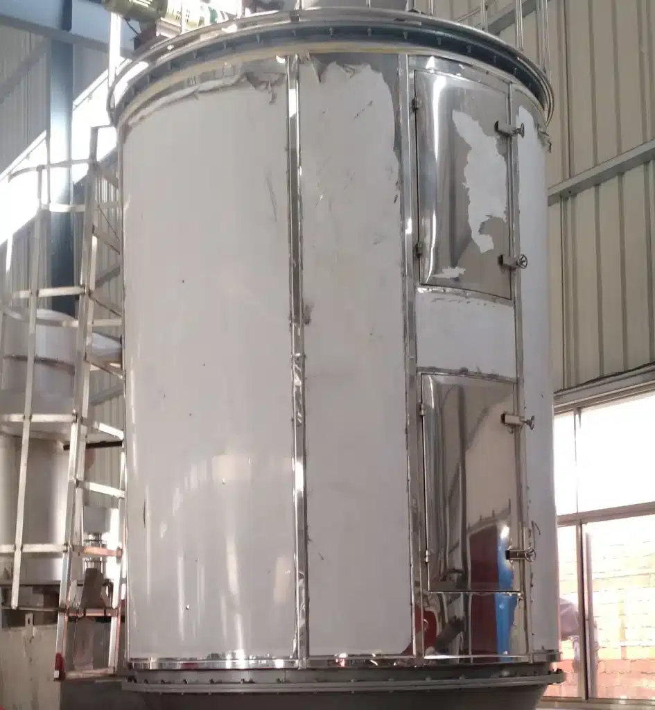An industrial Plate Dryer with a vertical cylindrical design, featuring internal drying plates, mounted on a solid base with various pipes and a motor, set in a workshop environment.