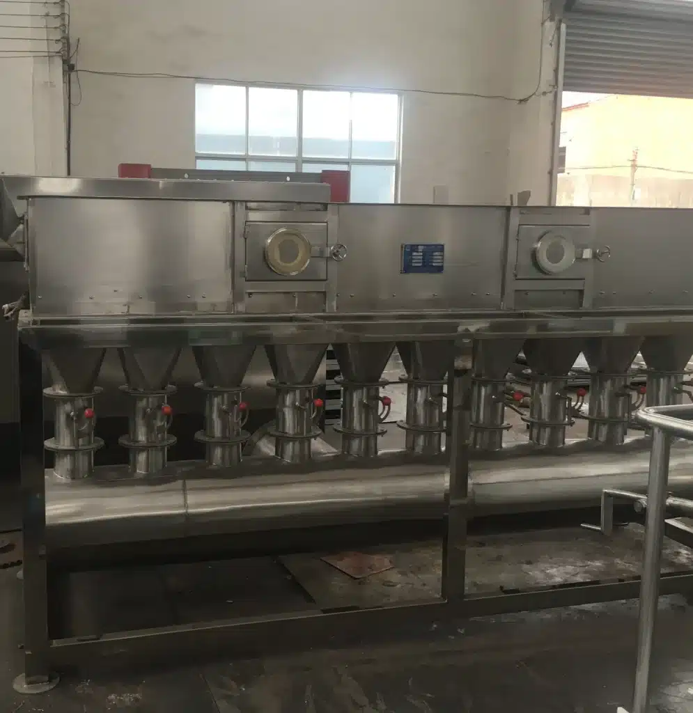 A Horizontal Fluidized Bed Dryer in an industrial setting, with multiple conical structures beneath a long horizontal chamber, indicative of fluidized drying technology, all constructed from polished stainless steel.