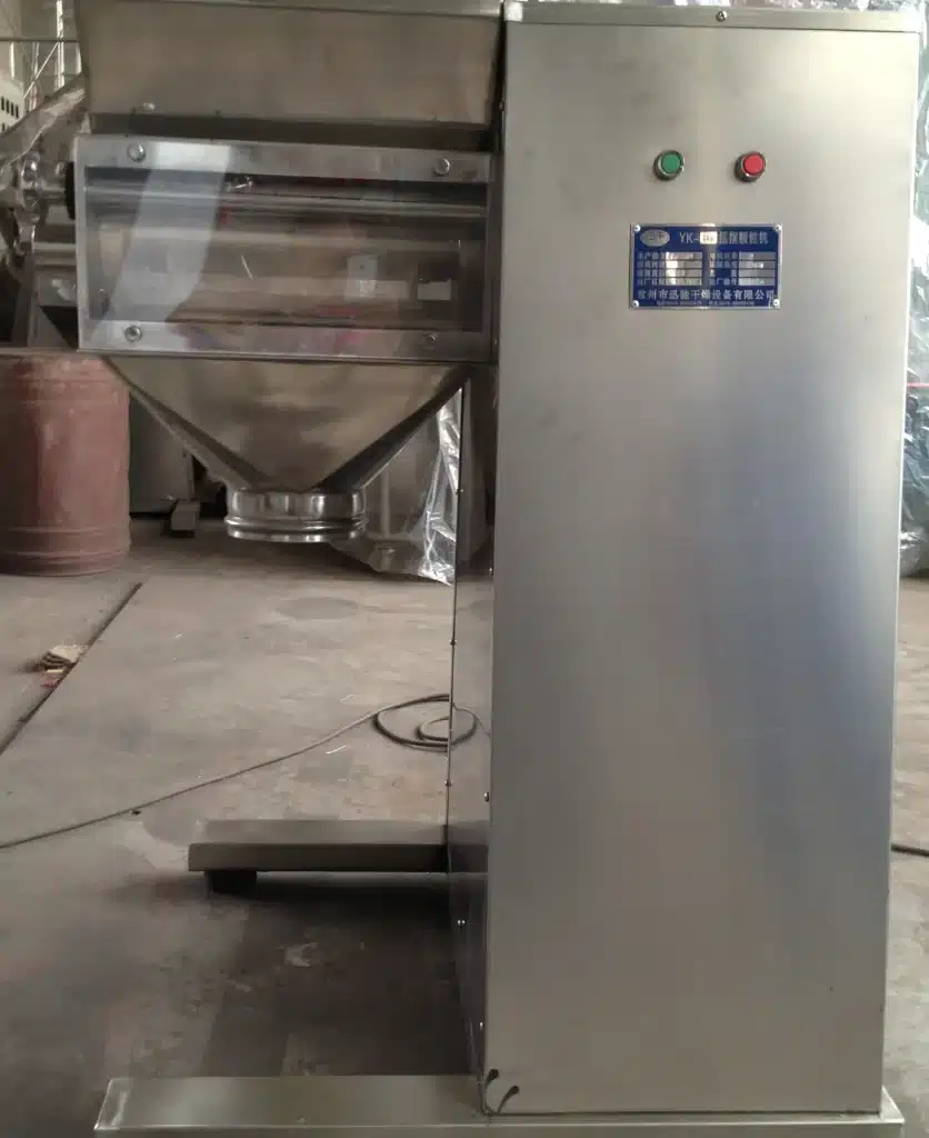 An Oscillating Granulator with a stainless steel body, control buttons, and a transparent protective cover, situated in an industrial setting.