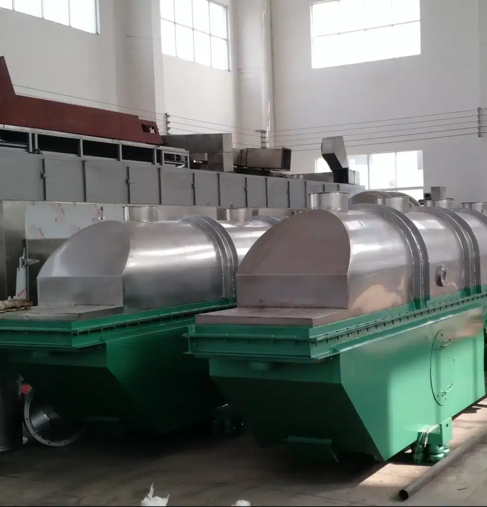 A large Vibrating Fluid Bed Dryer inside an industrial workshop, with a long green body and multiple silver dome-covered sections for drying particulates through vibration and fluidization, indicating a continuous drying process.