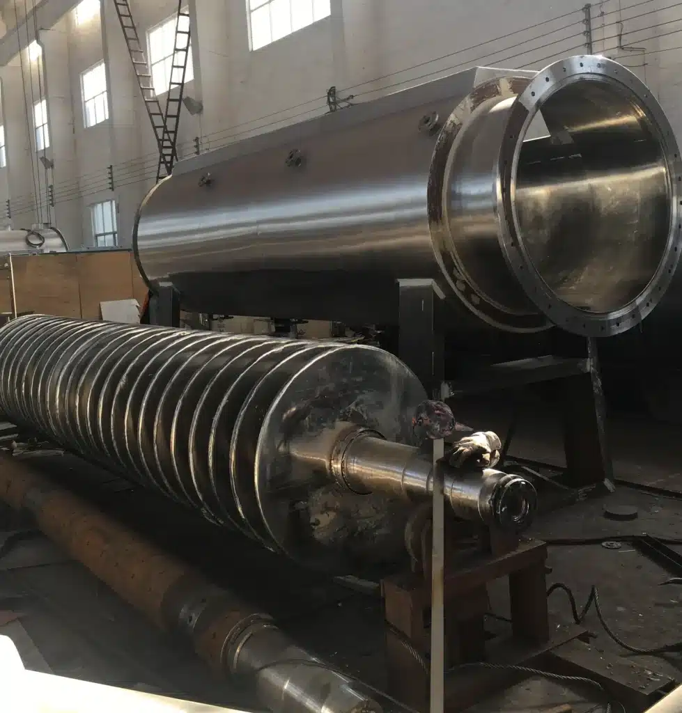 A large Disc Dryer in an industrial setting, with a stainless steel cylindrical body and a spiral disc shaft, ready for assembly or maintenance.